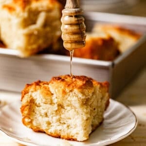 a butter swim biscuit on a plate with honey being drizzled on top.