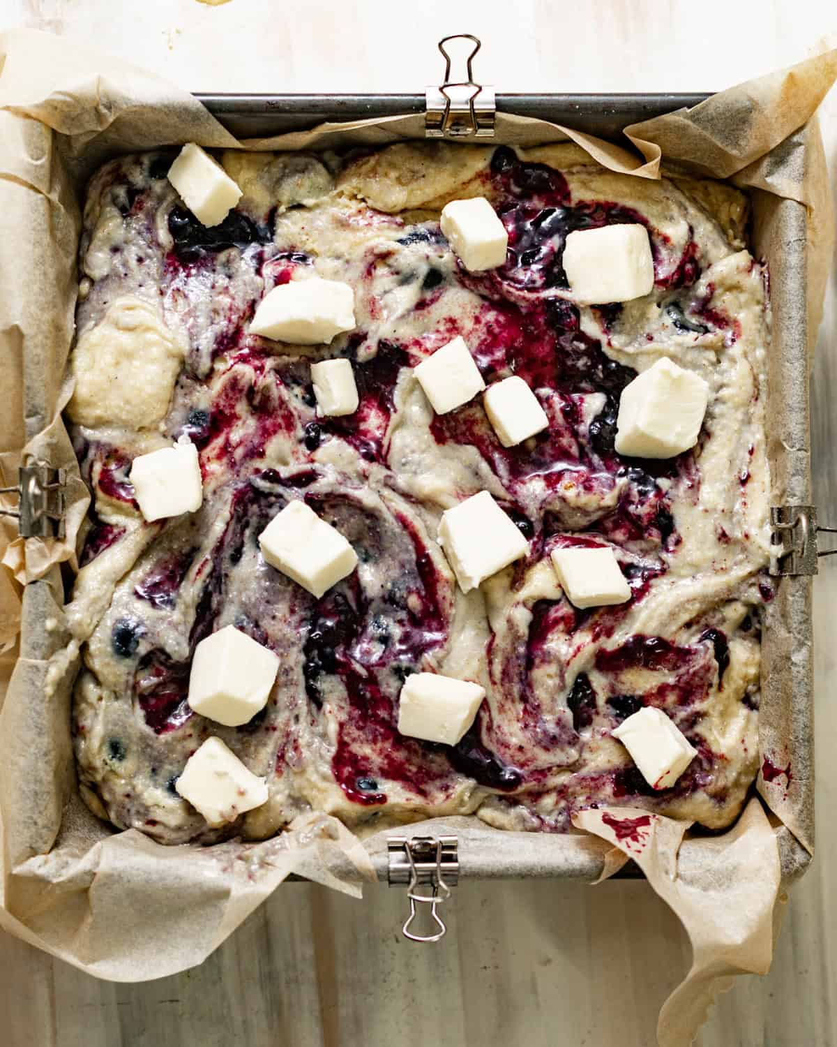 cornbread batter in a square baking dish with cubed butter and sprinkled sugar on top. 