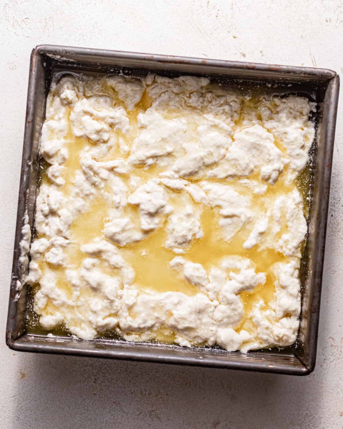biscuit dough in a square baking pan in a pool of melted butter.