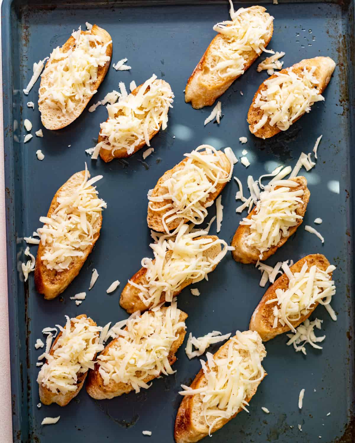 sliced baguette on a baking sheet topped with steak pan drippings and shredded mozzarella. 