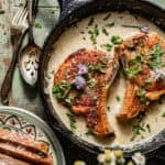 pan seared pork chops in a skillet with a garlic butter sauce on top.