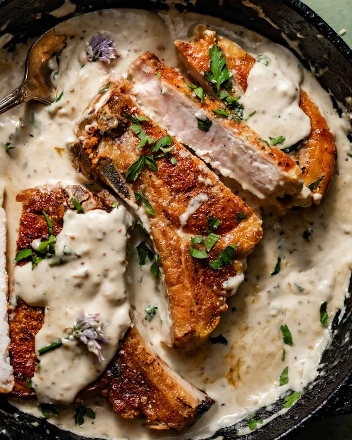 sliced pork chops in a skillet covered in creamy garlic butter sauce.