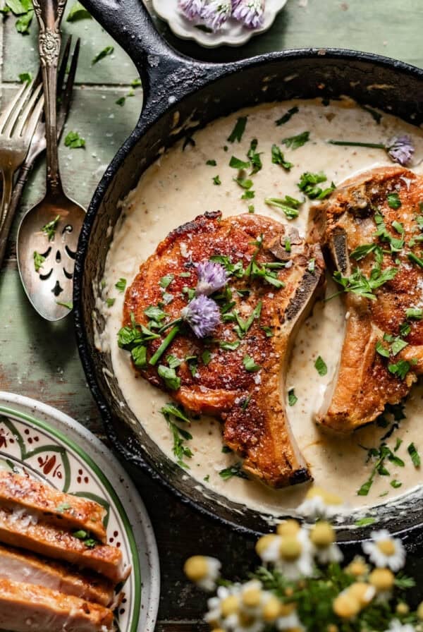 pan seared pork chops in a skillet with a garlic butter sauce on top.