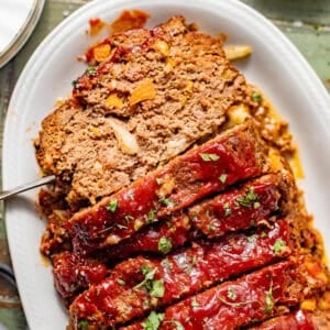 sliced bbq meatloaf on a serving plate garnished with fresh parsley.