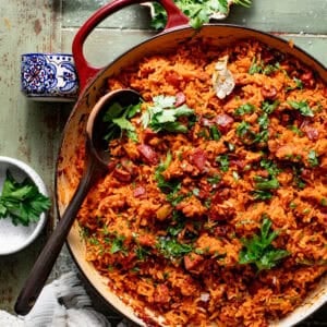 gullah red rice in a pot topped with fresh parsley with a wooden spoon scooping the rice.