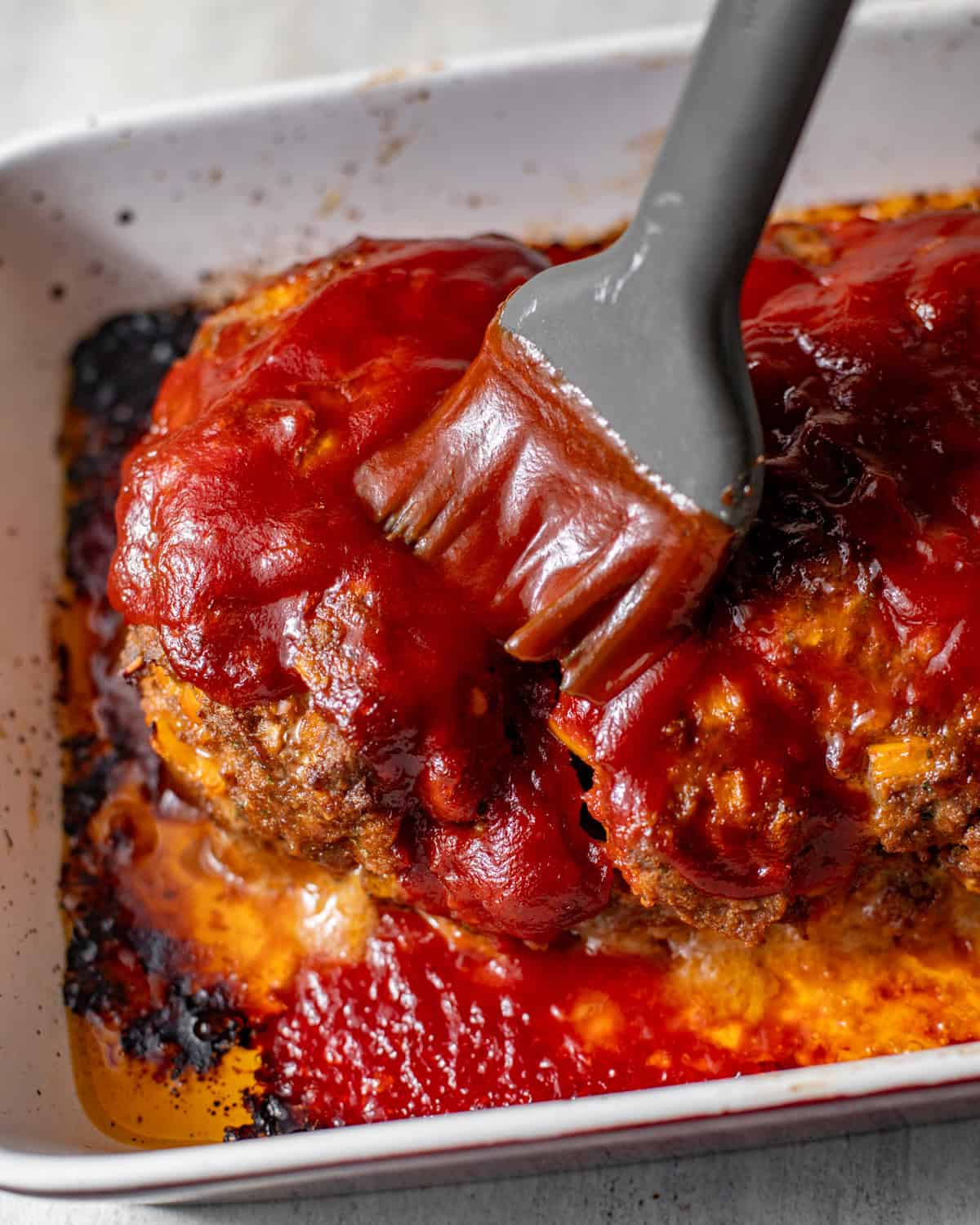 a bbq brush brushing the bbq glaze on top of the meatloaf.