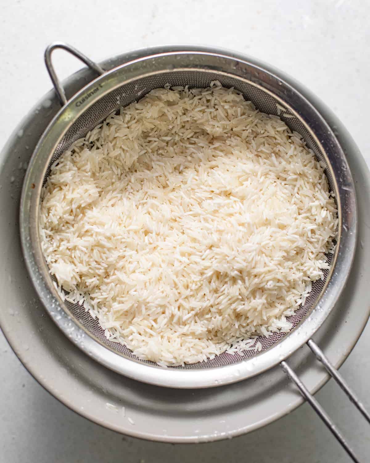 rice on top of a bowl being rinsed through a sieve.