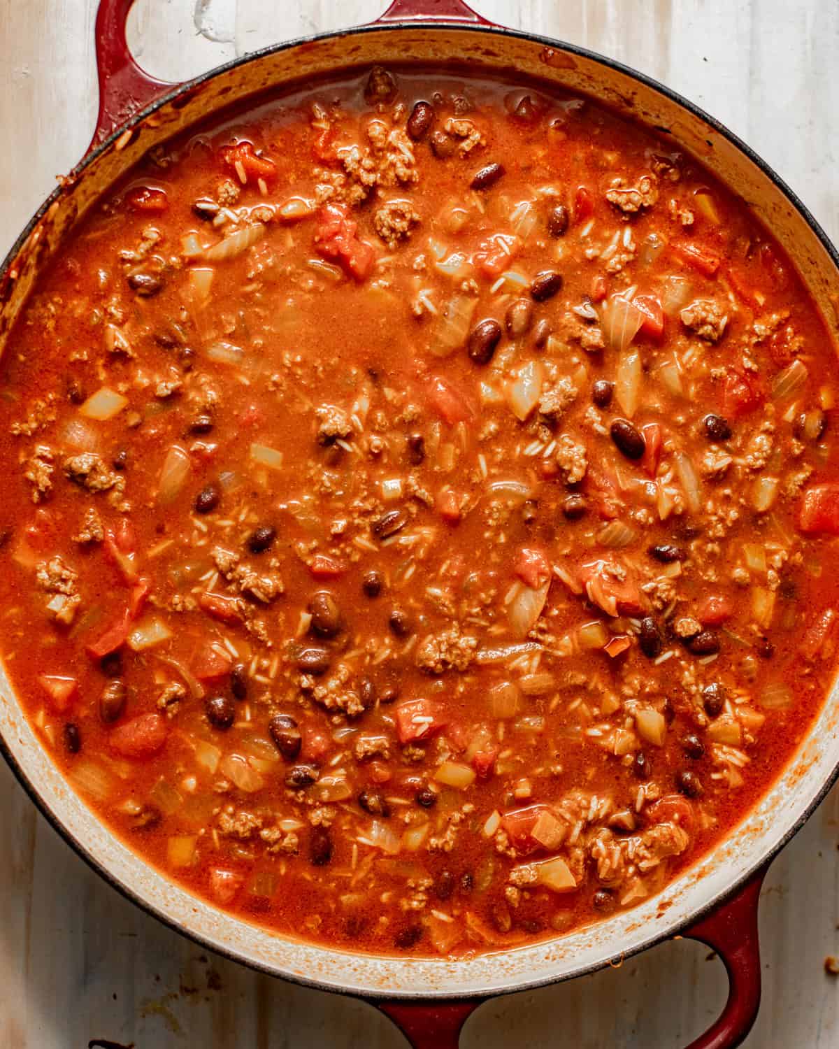 cooked ground beef with rice and veggies in a large skillet with tomatoes, beef broth, and black beans.