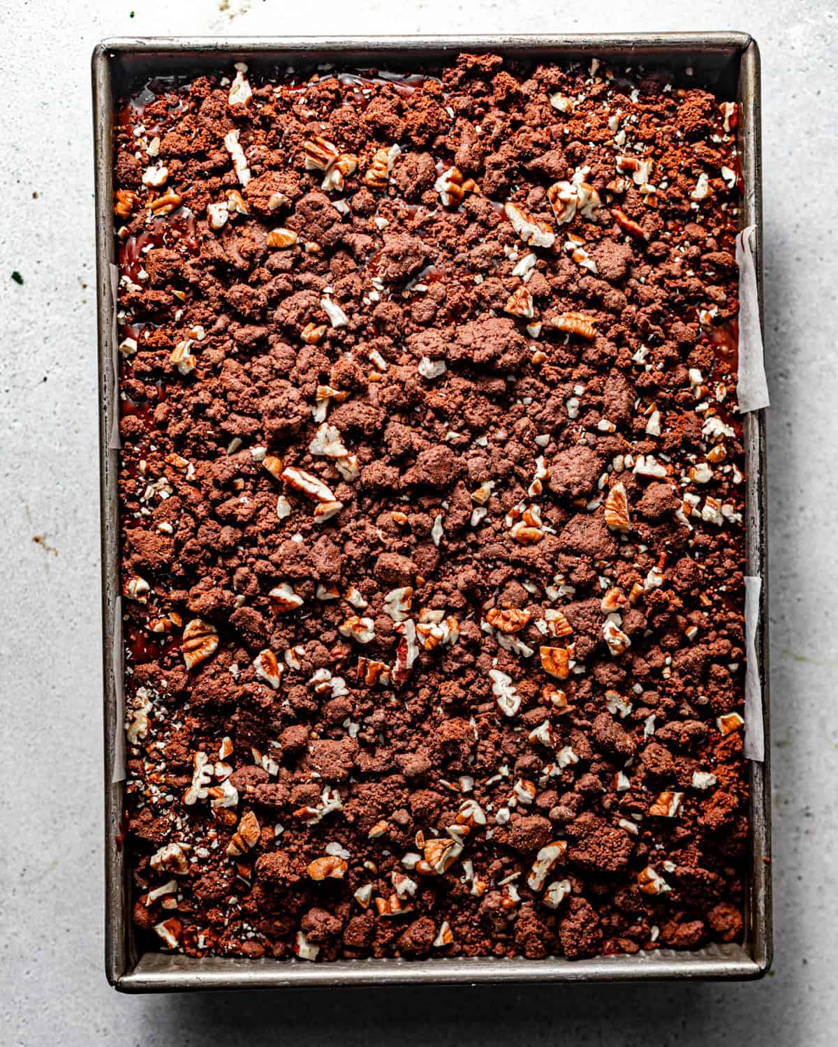 texas chocolate sheet cake in a baking pan topped with fudge frosting and chocolate crunch and chopped pecans.