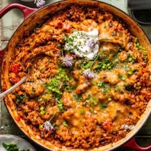 taco rice in a large skillet topped with sour cream, cheese, and diced chives and green onions.
