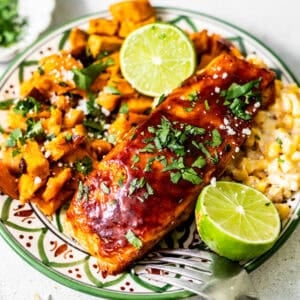 bbq salmon on a plate with sweet potatoes and corn and garnish with a lime and fresh parsley.