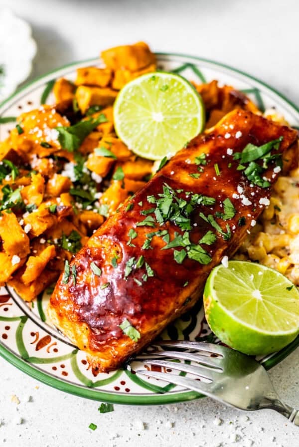 bbq salmon on a plate with sweet potatoes and corn and garnish with a lime and fresh parsley.