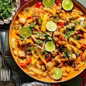 chicken fajita pasta in a large skillet topped with cilantro and sliced limes.