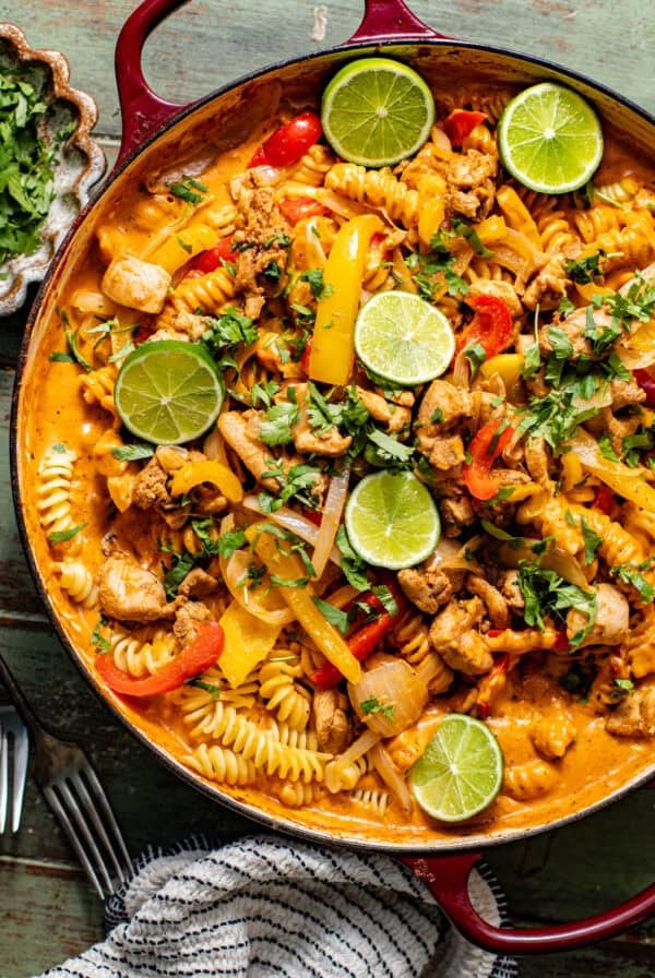 chicken fajita pasta in a large skillet topped with cilantro and sliced limes.