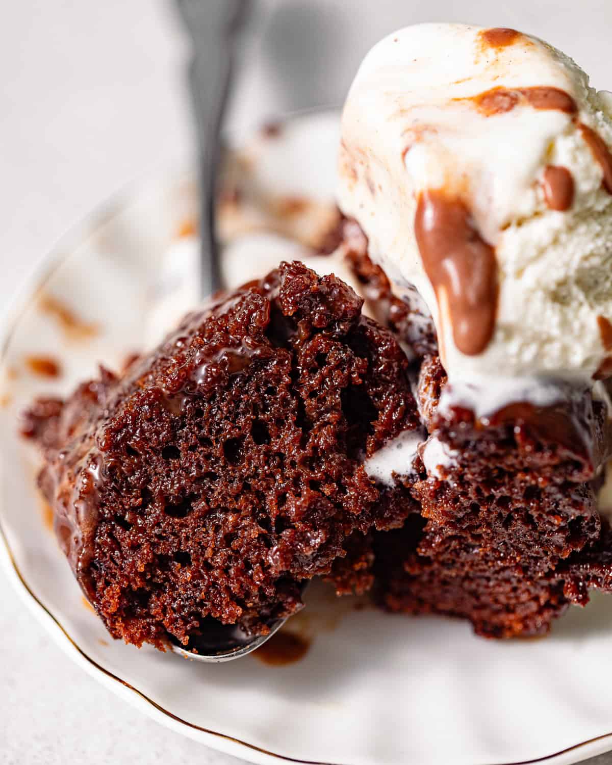 a bite size piece of chocolate sticky toffee pudding on a spoon with ice cream.