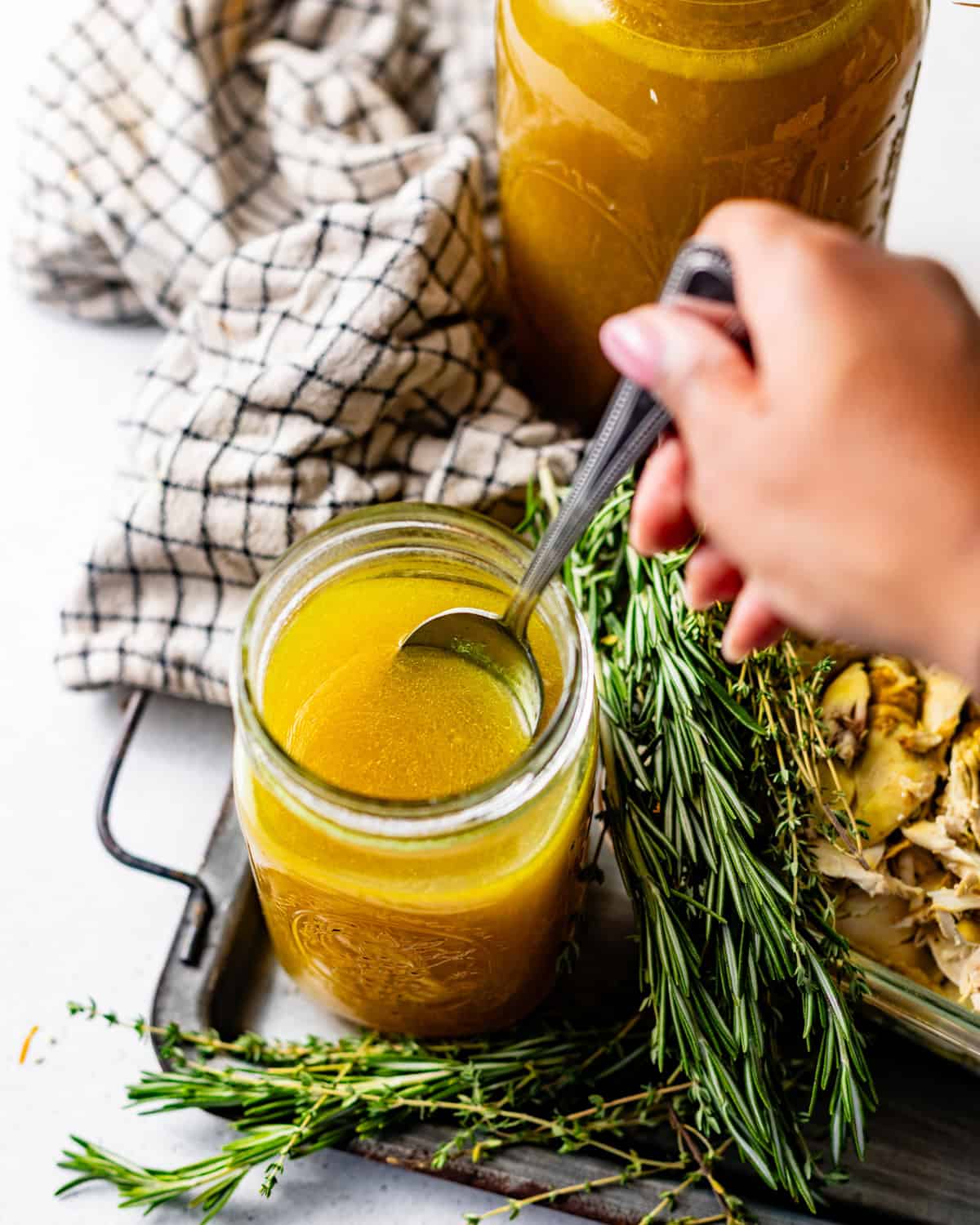 a hand using a spoon to scoop the chicken broth out of the jar.