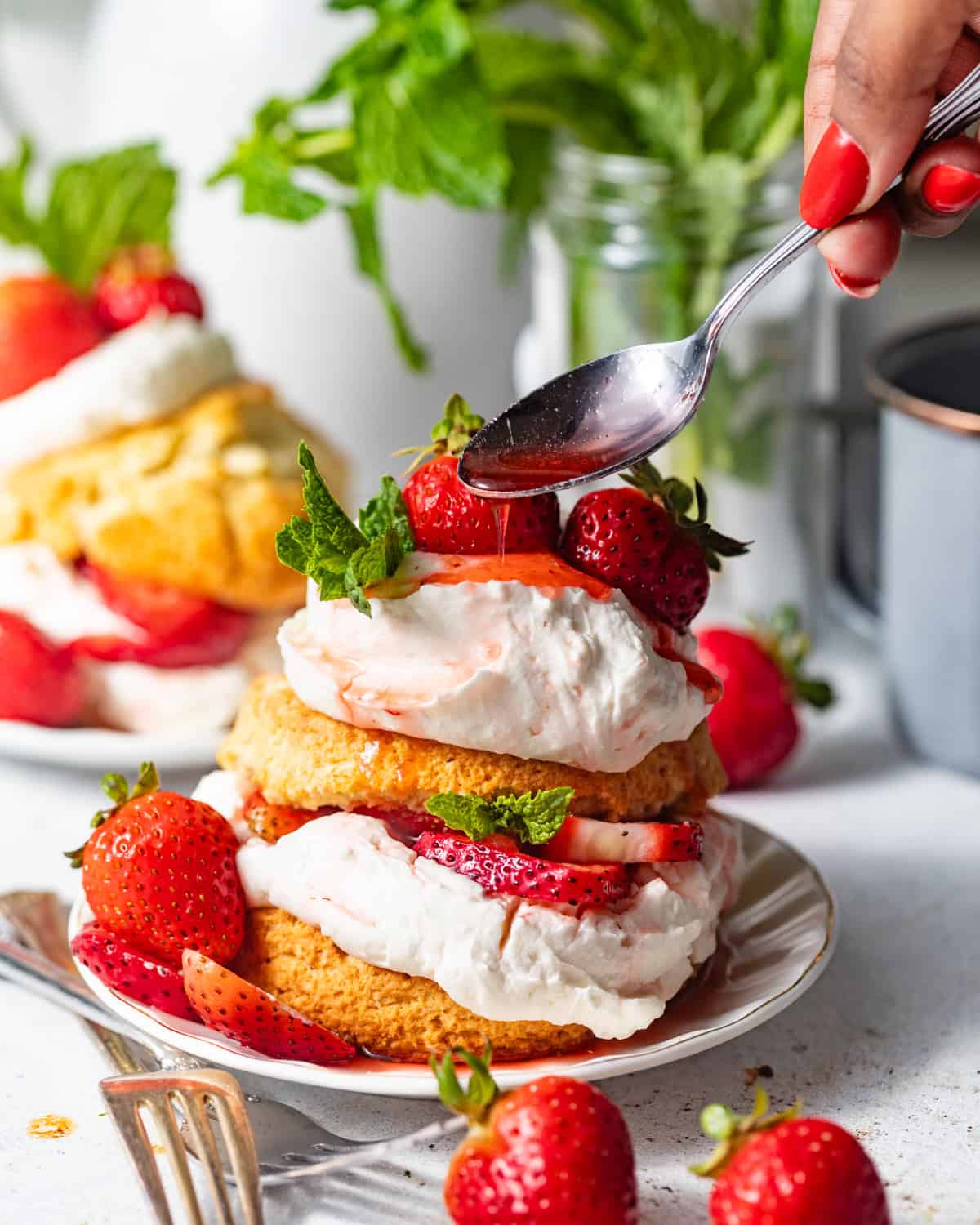 strawberry shortcake on a small plate with strawberry syrup being poured on top. 