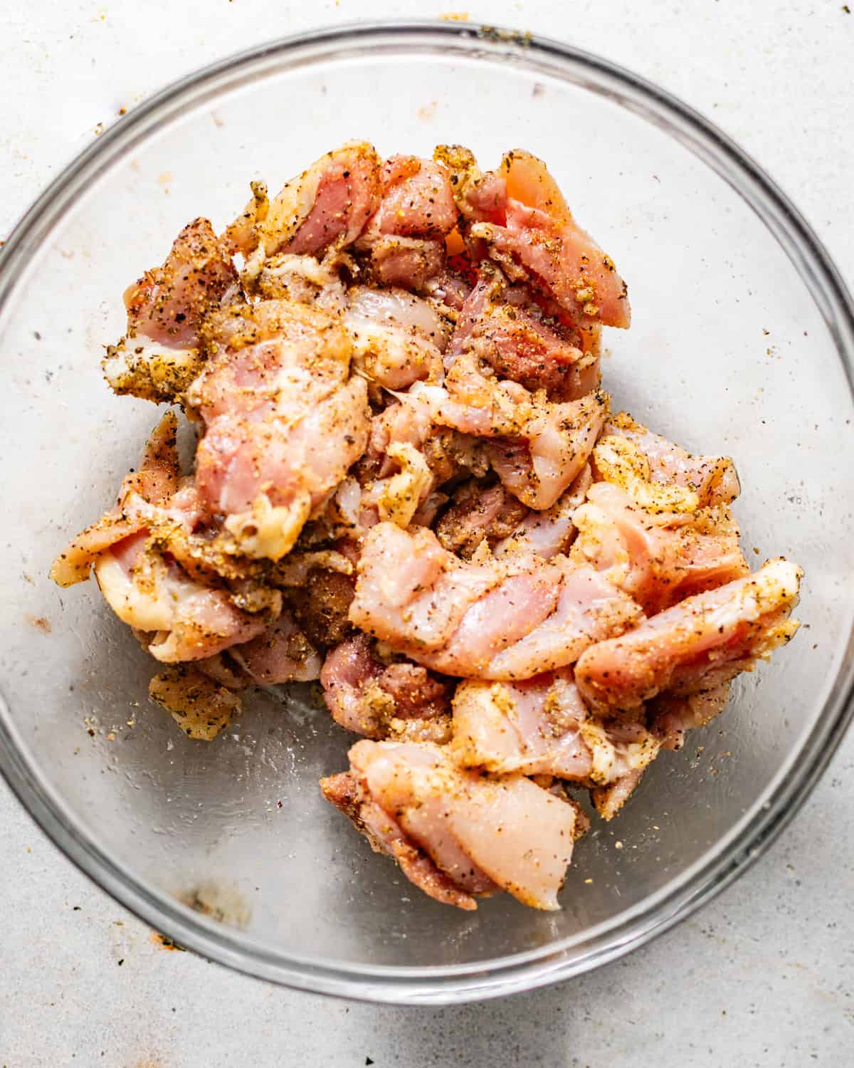chicken thighs cut into bite sized chunks and coated in seasonings in a bowl. 