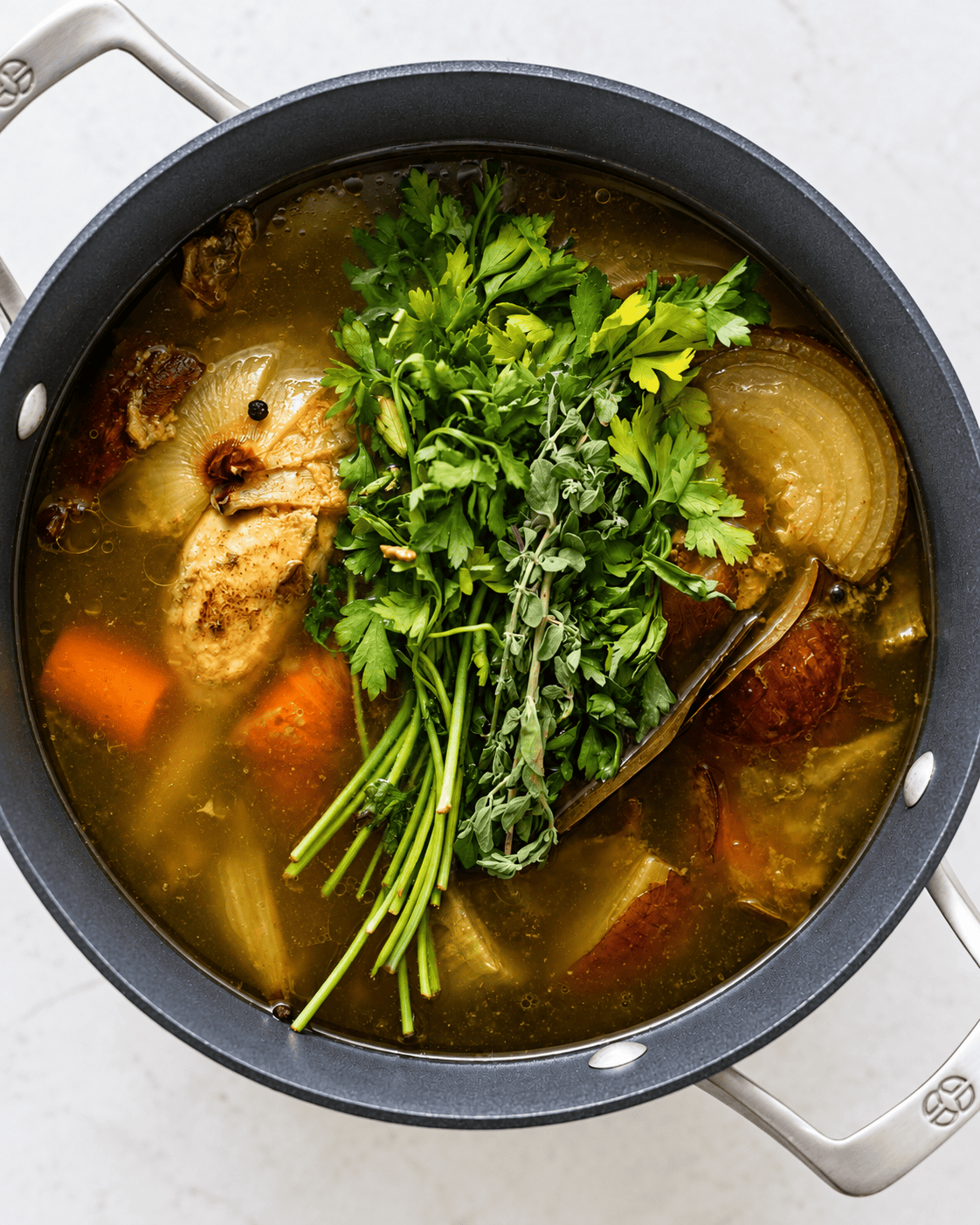 homemade chicken broth simmering with a whole chicken, vegetables, and fresh herbs.