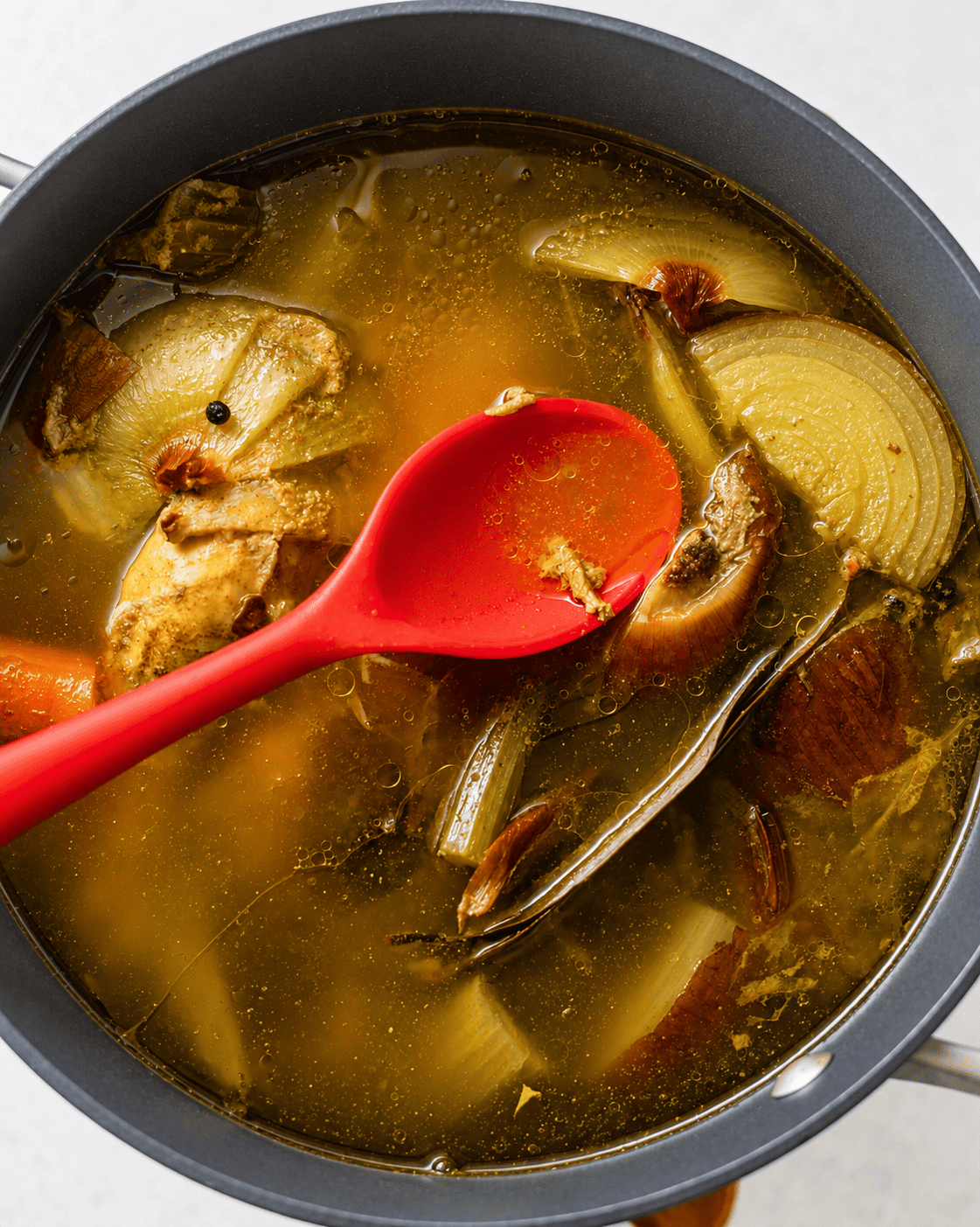 a spoon removing the foam off of the top of the chicken broth while the broth is simmering in a pot.