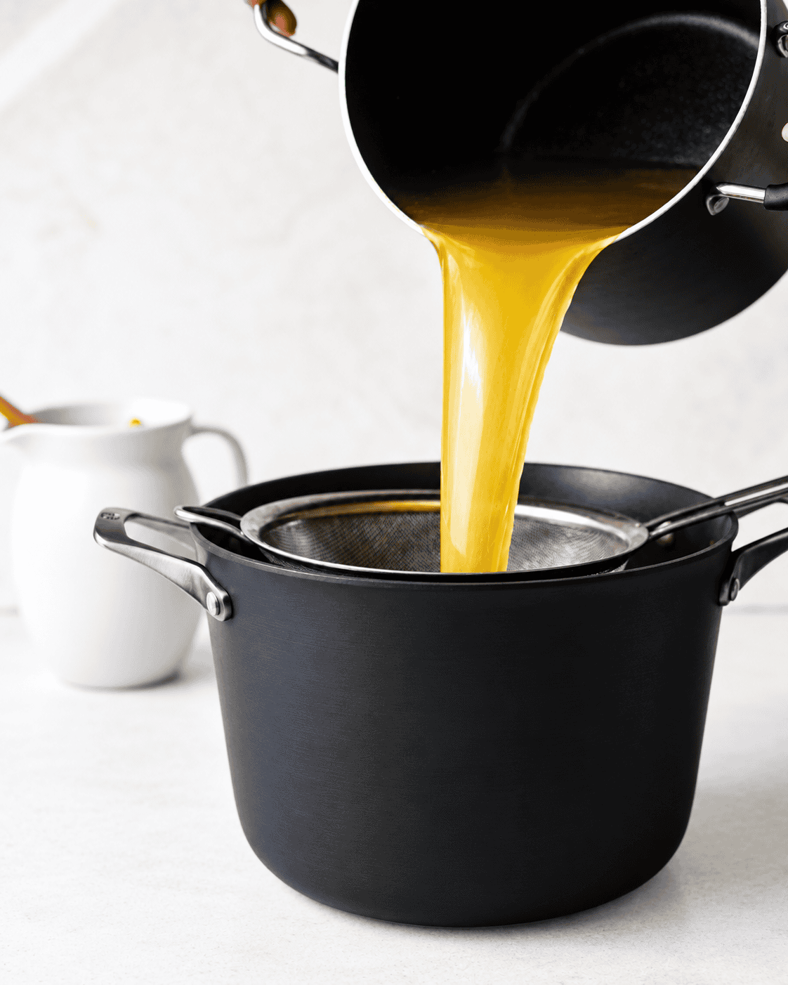 Homemade chicken broth being poured through a fine-mesh strainer into a large pot.