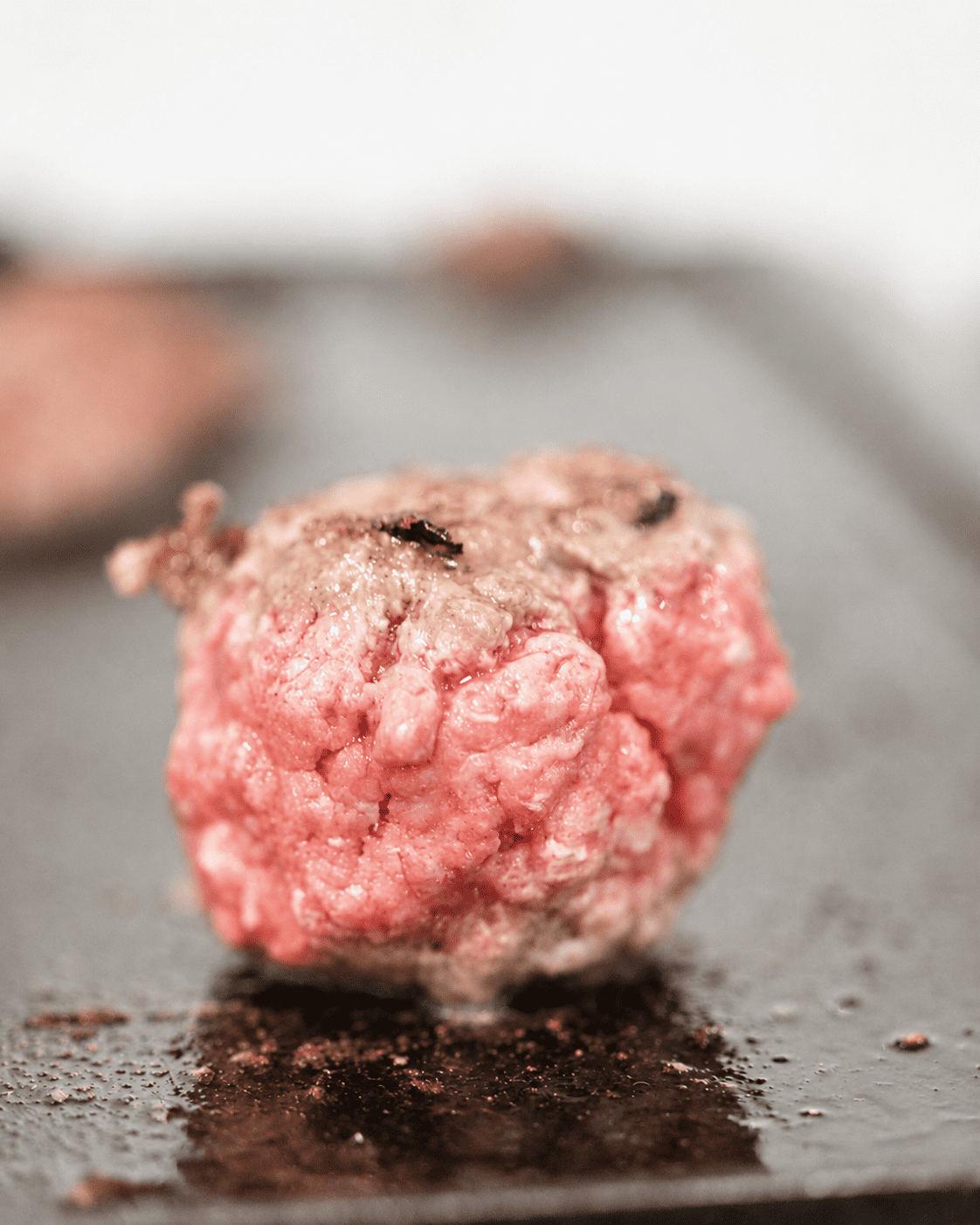 a ball of ground beef on a hot griddle before smashing with a burger press.