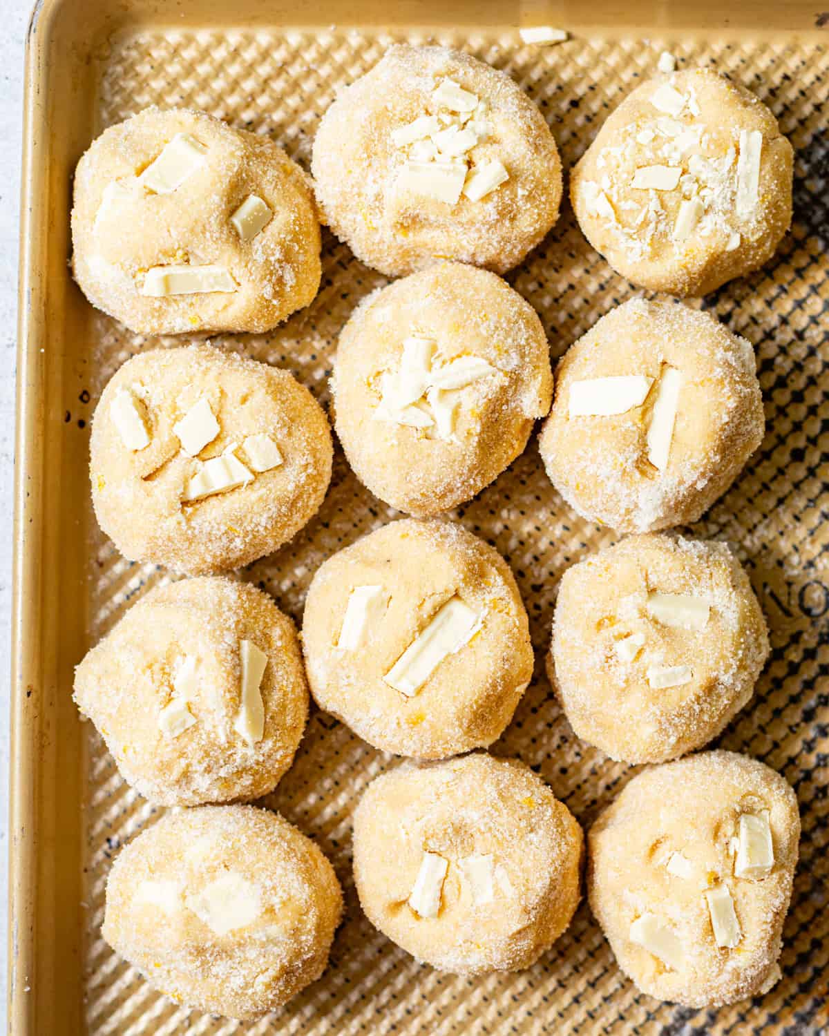cookie dough balls on a baking sheet with white chocolate chunks pressed into the tops of the cookies.