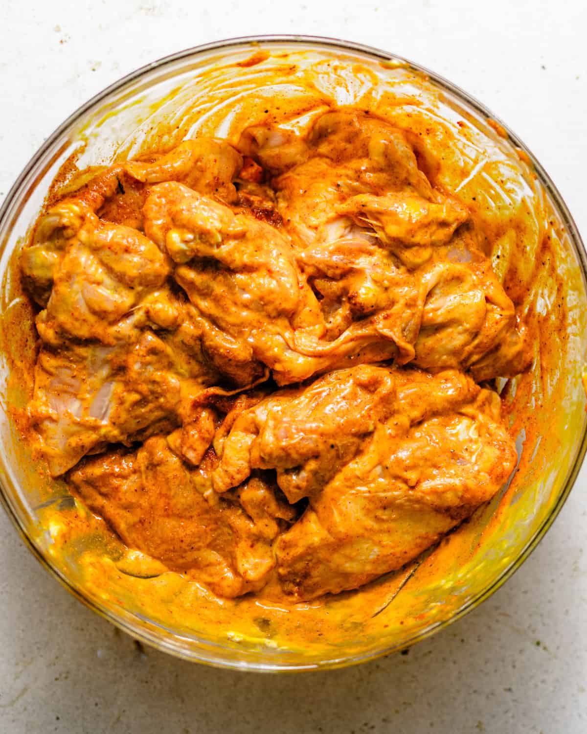 chicken thighs in a mixing bowl coated in seasonings and chicken marinade.