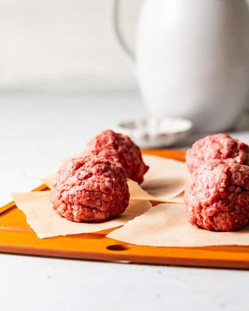 ground beef rolled into balls and placed onto parchment paper.