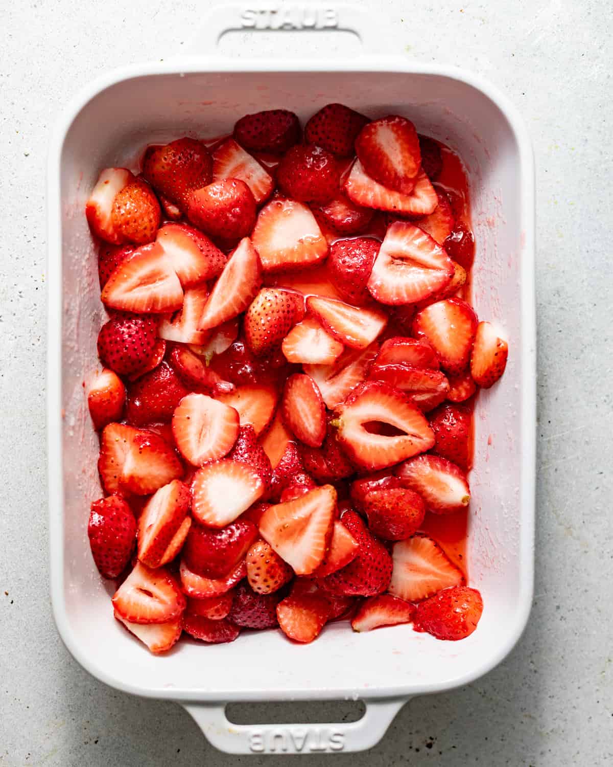sliced strawberries in a pan tossed in sugar, lemon juice, and strawberry preserves.