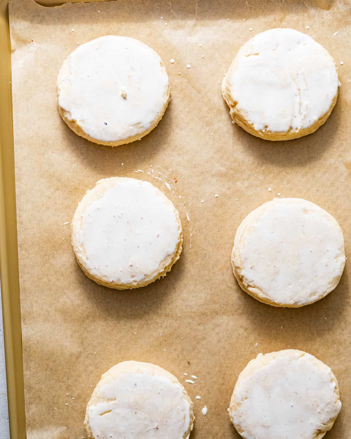 biscuits on a parchment paper lined baking sheet brushed with heavy cream and sugar sprinkled on top before baking. 