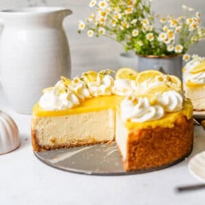 lemon cheesecake with lemon curd on a white surface with edible flowers on top.