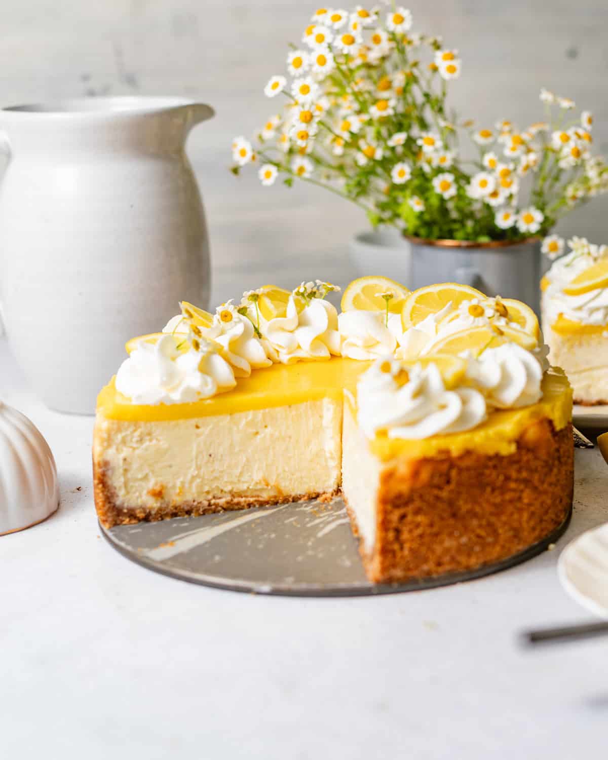 lemon cheesecake with lemon curd on a white surface with edible flowers on top.
