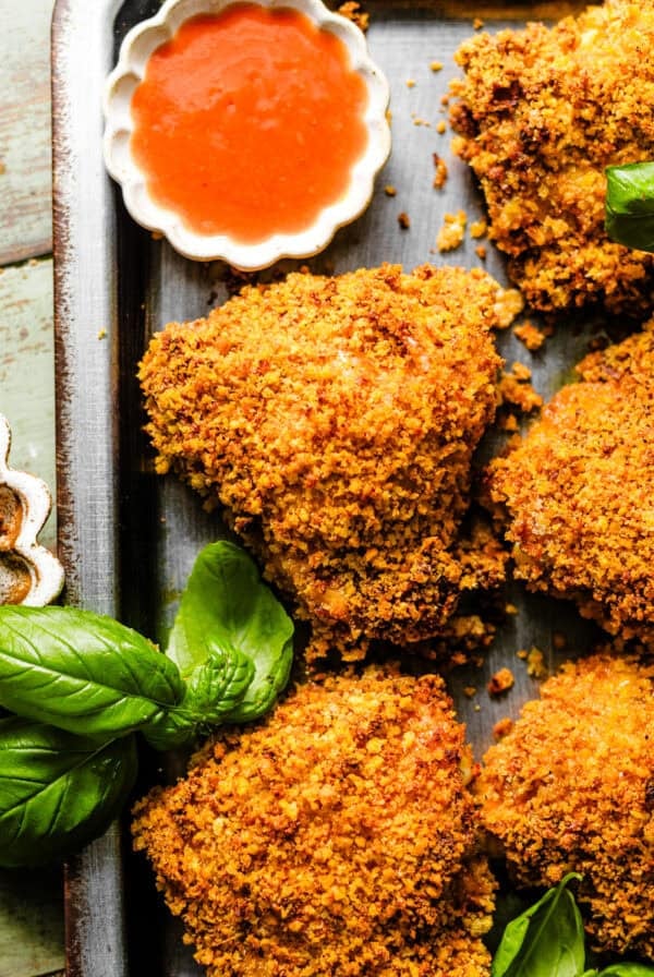 crispy oven fried chicken on a serving tray with a small bowl of hot sauce.