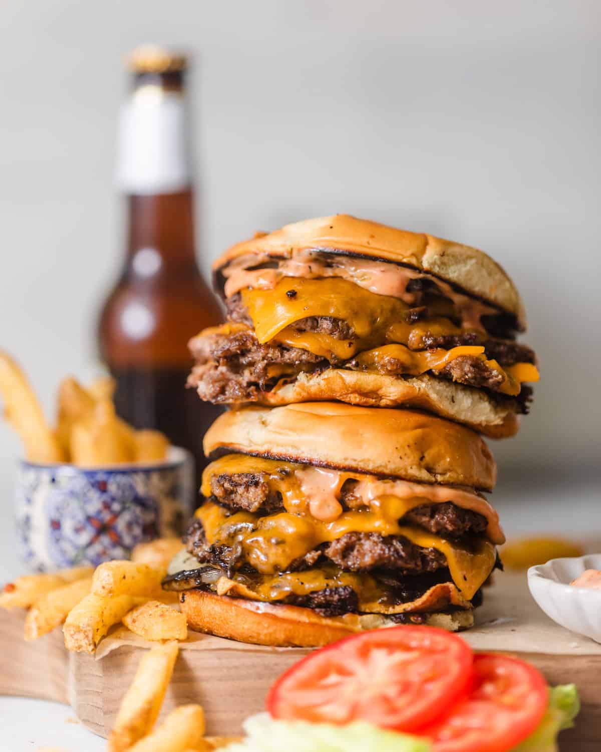 smash burgers stacked on top of each other on a serving board with french fries, lettuce, and tomato on the side.