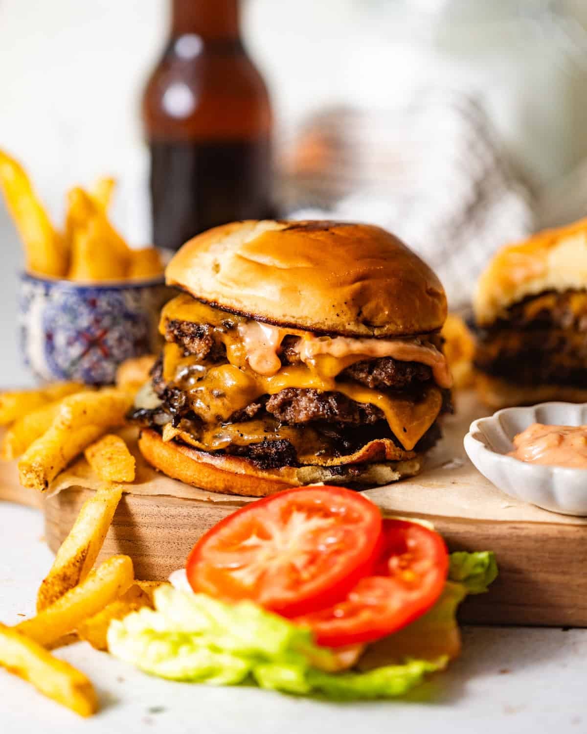 homemade smash burgers on a serving board with lettuce, tomatoes, and french fries on the side.