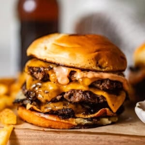 smash burger on a wooden board topped with fried onions, melted cheese, and burger sauce.