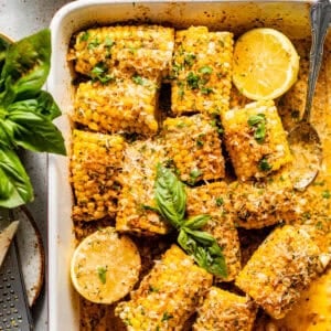 baked corn on the cob in a baking dish covered in garlic butter and fresh herbs.
