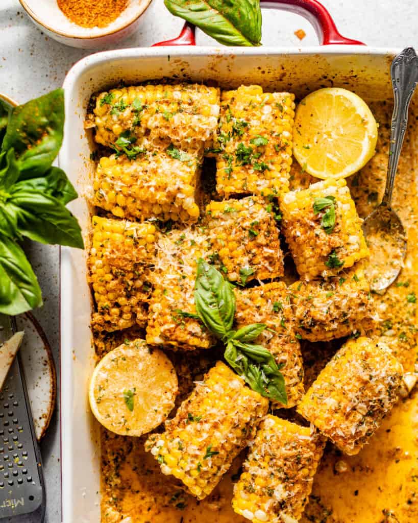 baked corn on the cob in a baking dish covered in garlic butter and fresh herbs.