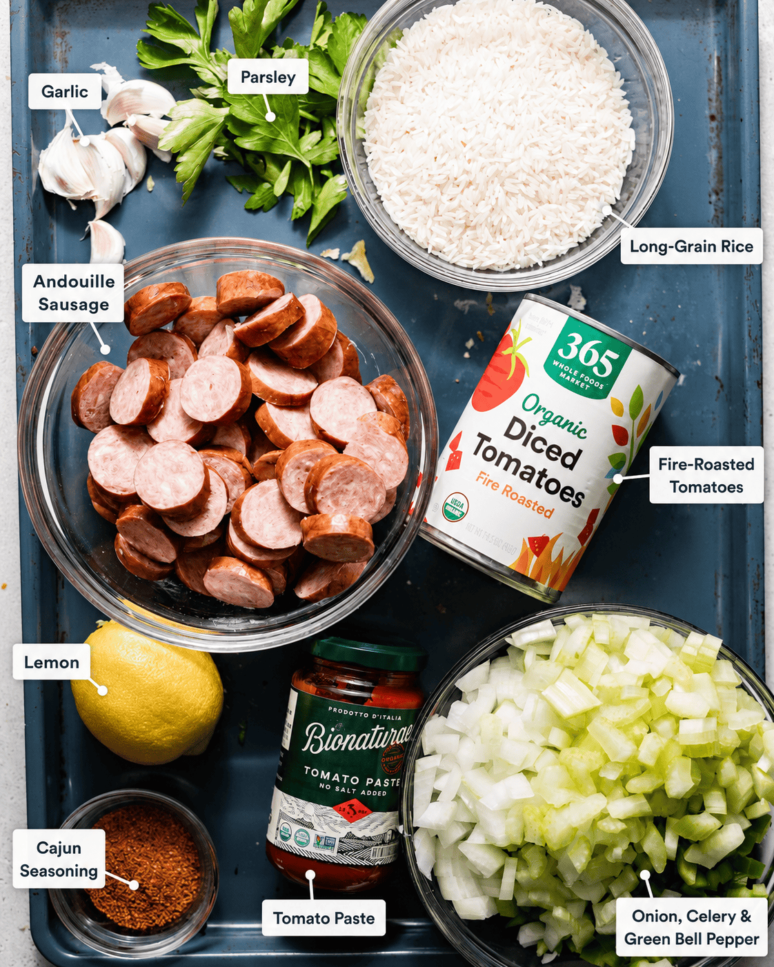 ingredients to make cajun sausage and rice skillet - andouille, onion, celery, green bell pepper, long grain rice, diced tomatoes, lemon juice, seasonings, garlic, tomato paste, and chicken broth.