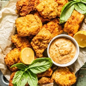 crispy catfish nuggets on a serving tray with Cajun tartar sauce with lemon wedges and fresh herbs on top for garnish.