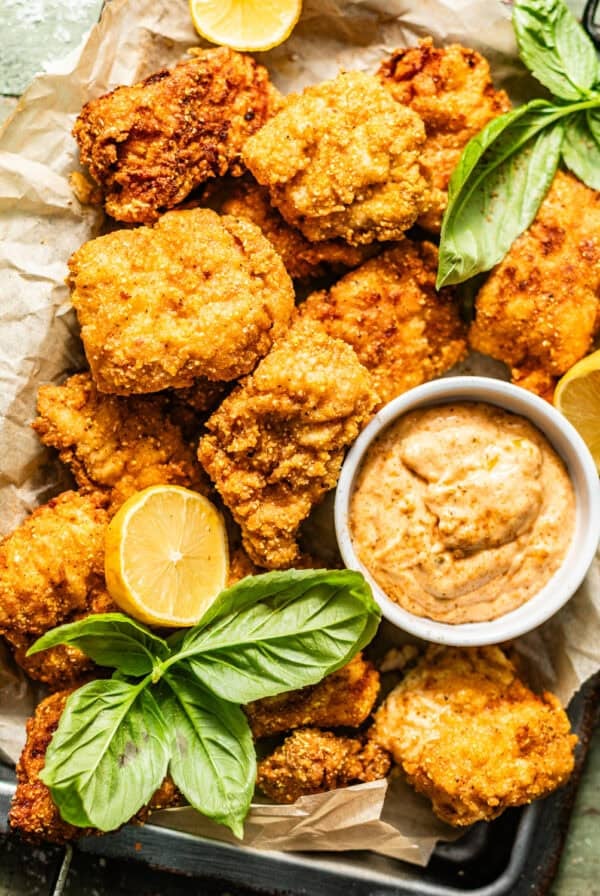 crispy catfish nuggets on a serving tray with Cajun tartar sauce with lemon wedges and fresh herbs on top for garnish.