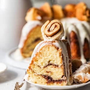 a slice of cinnamon roll pound cake on a cake plate topped with a mini cinnamon roll.