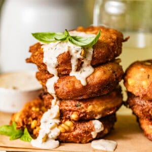 crispy corn fritters stacked on top of each other with dipping sauce drizzled down the sides.