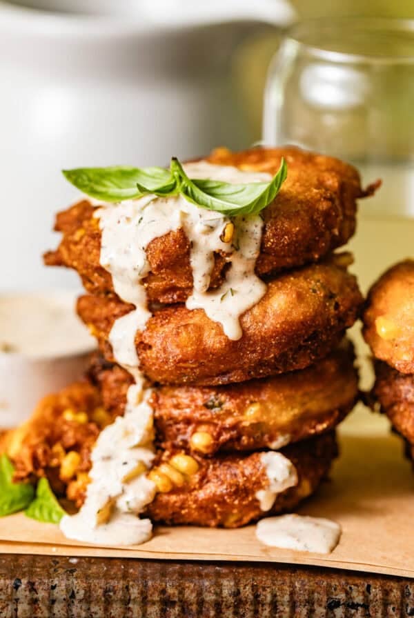 crispy corn fritters stacked on top of each other with dipping sauce drizzled down the sides.