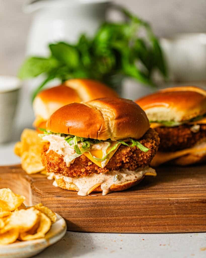fried fish sandwiches on a serving board with a bowl of potato chips on the side.