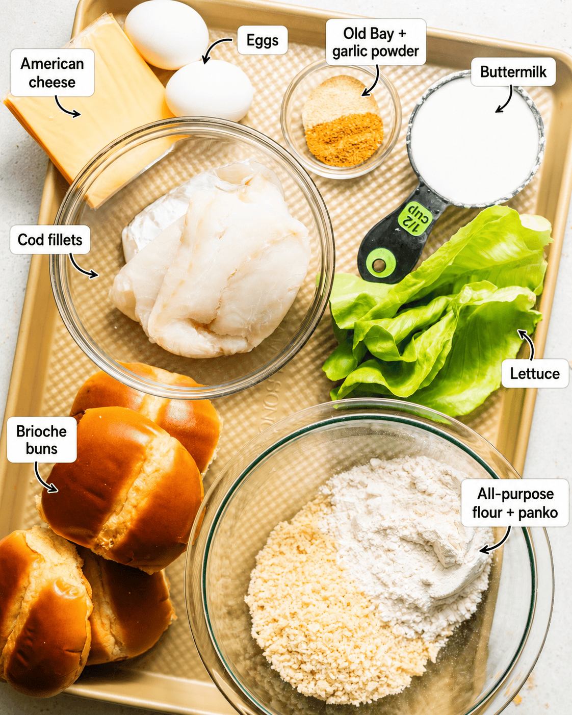 ingredients to make fried fish sandwiches on a baking sheet - cod, american cheese, lettuce, brioche buns, buttermilk, eggs, panko breadcrumbs, flour, and seasonings.