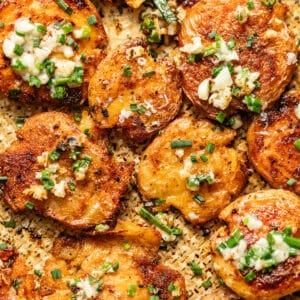 garlic parmesan smashed potatoes on a baking sheet topped with garlic butter.