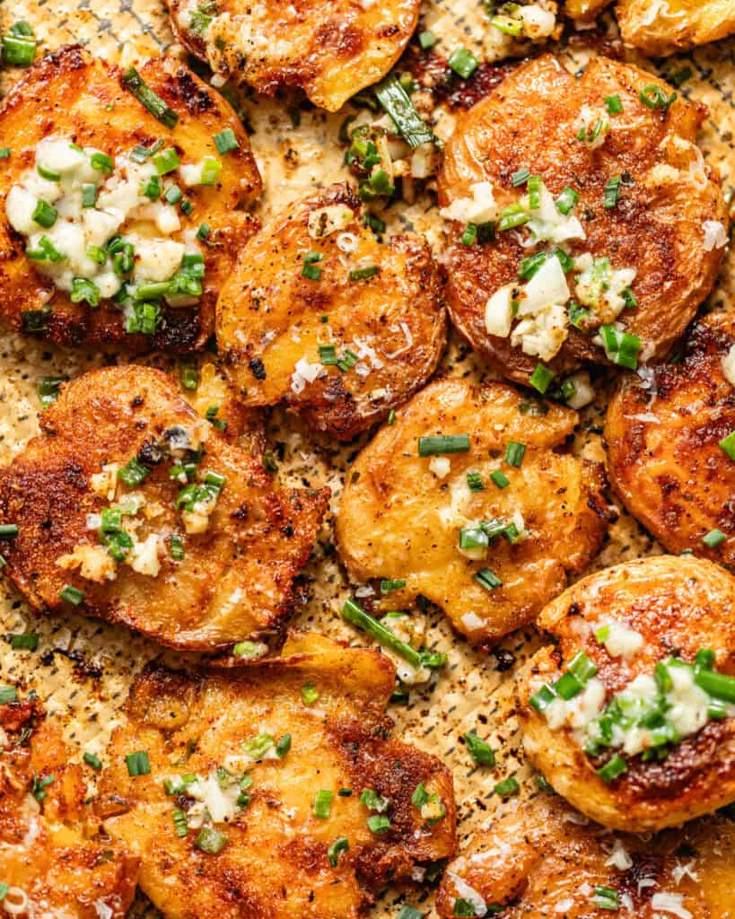 garlic parmesan smashed potatoes on a baking sheet topped with garlic butter.
