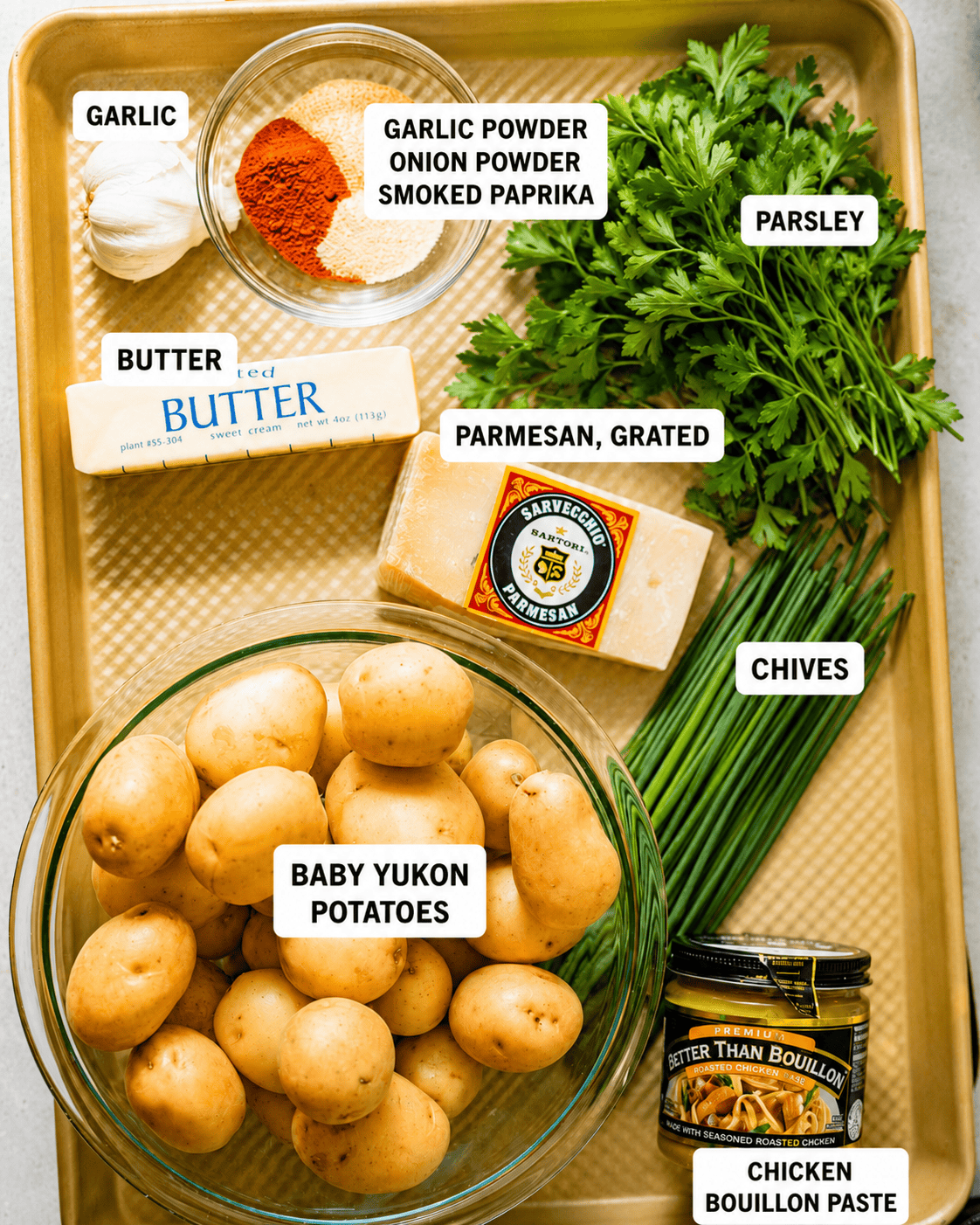 ingredients to make garlic smashed potatoes on a baking sheet - baby potatoes, seasonings, chives, parsley, parmesan, butter, garlic, and chicken bouillon paste to boil the potatoes in.
